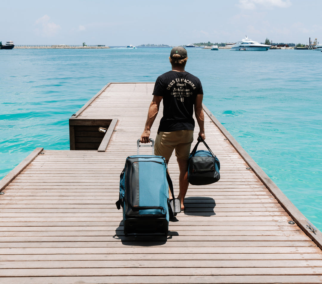 Man wheels 2 wheeled duffel down dock in Maldives