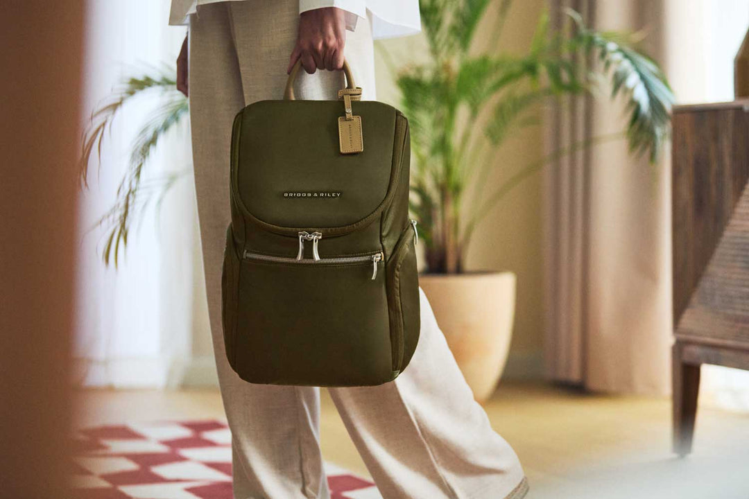 Woman carrys olive green briggs and riley rhapsody backpack through hotel lobby