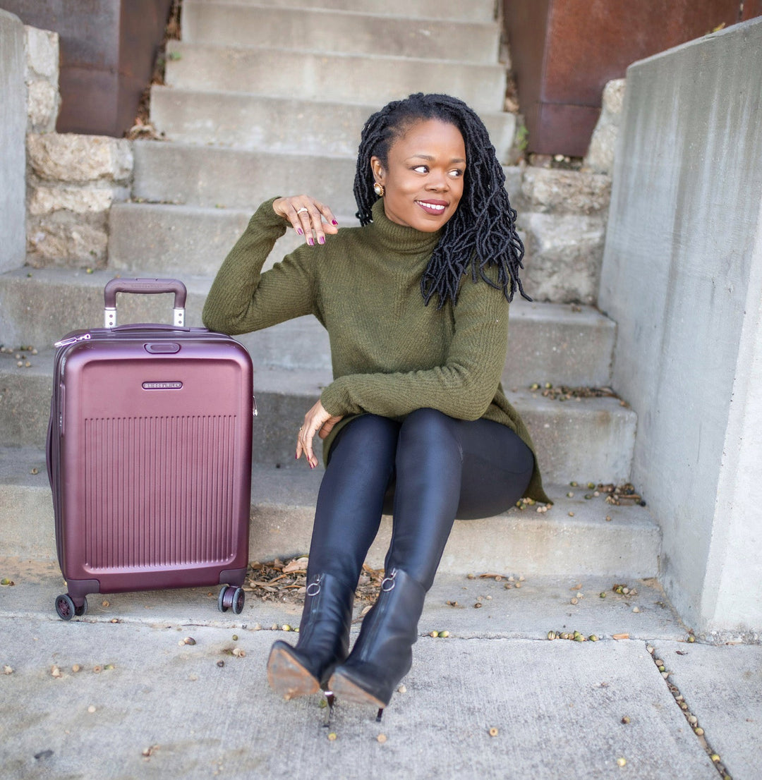 Woman sits on stairs with 4 wheel purple carry on suitcase