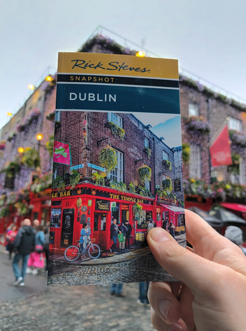 Man holding Rick Steves guidebook up to a corver store in Dublin