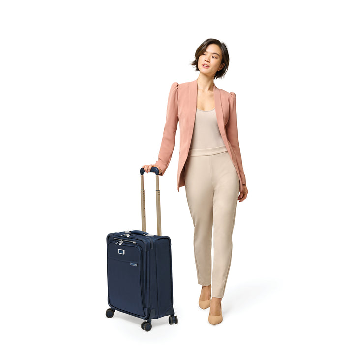 Female model in pink blazer wheels navy blue global international briggs and riley carry on suitcase