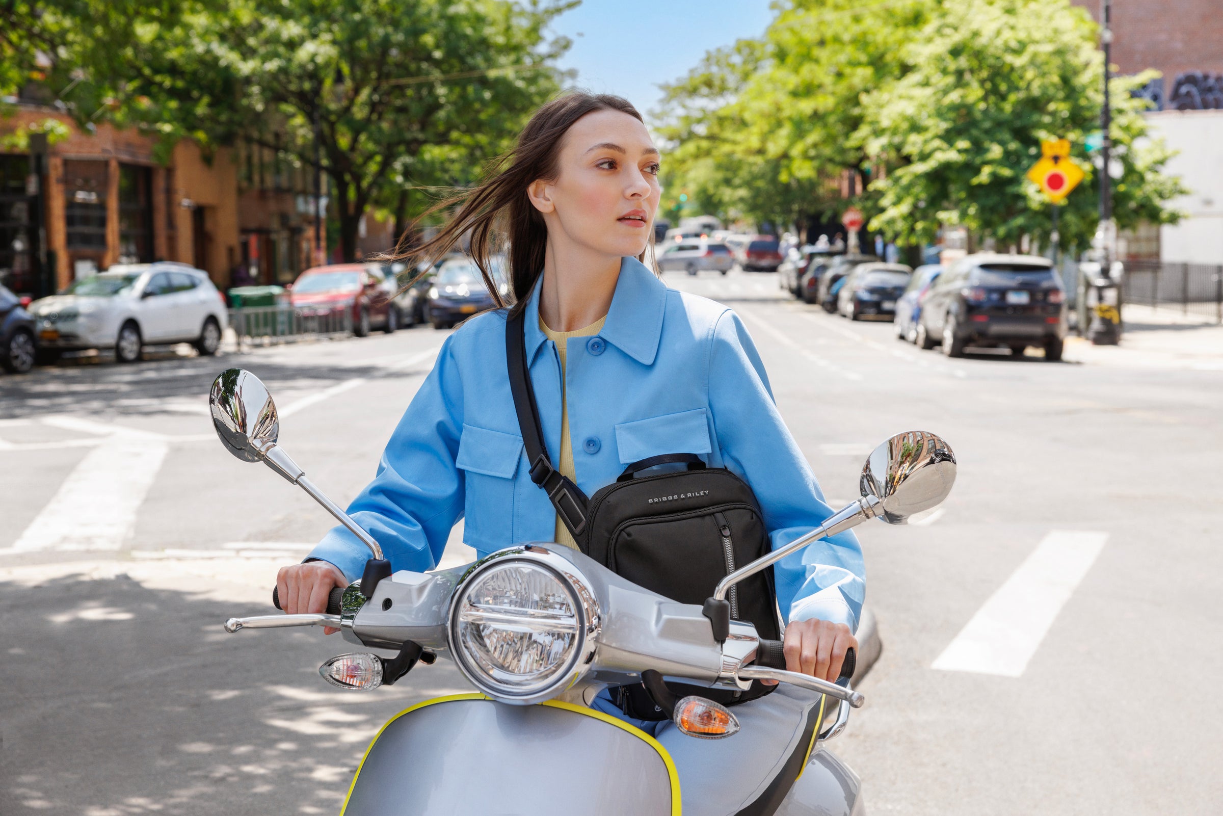 Woman riding moped through city with Briggs & Riley crossbody bag