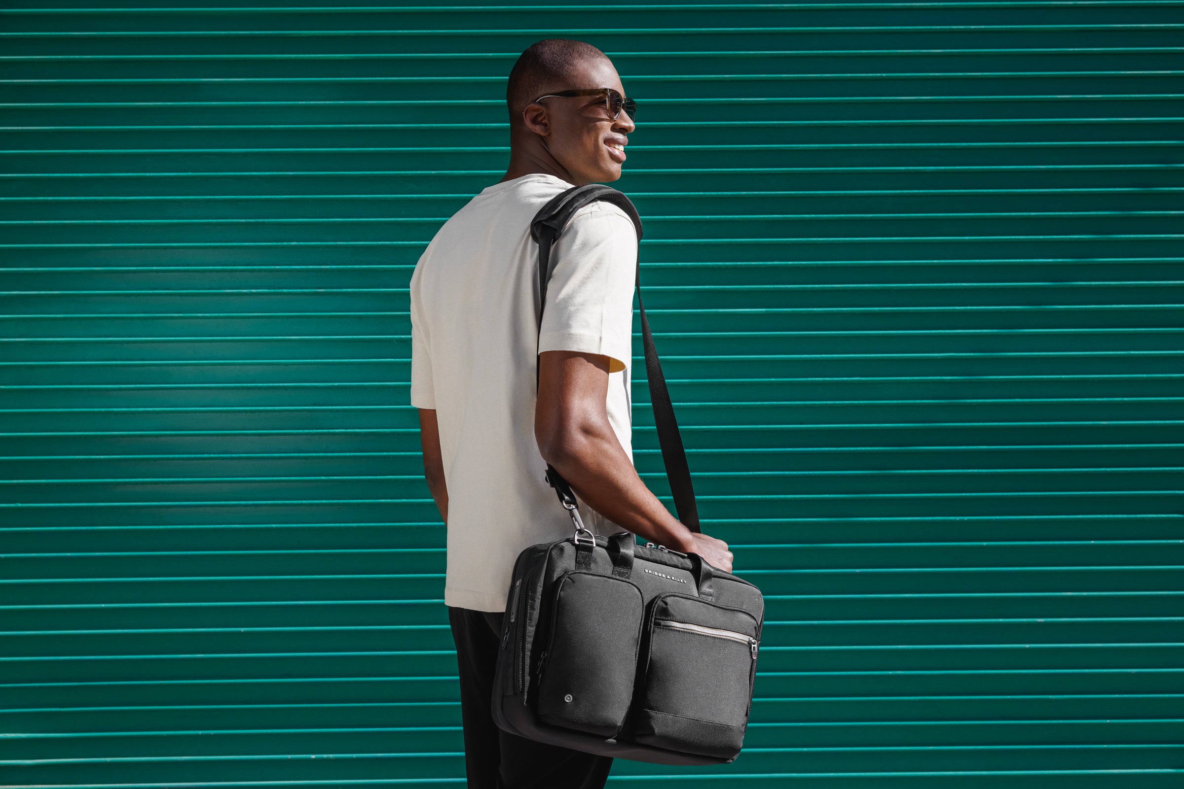 Man carries Briggs and Riley softside Briefcase on city street with teal wall in background