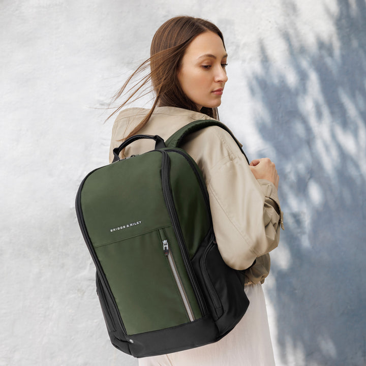 Woman walks down street with green briggs and riley medium widemouth backpack