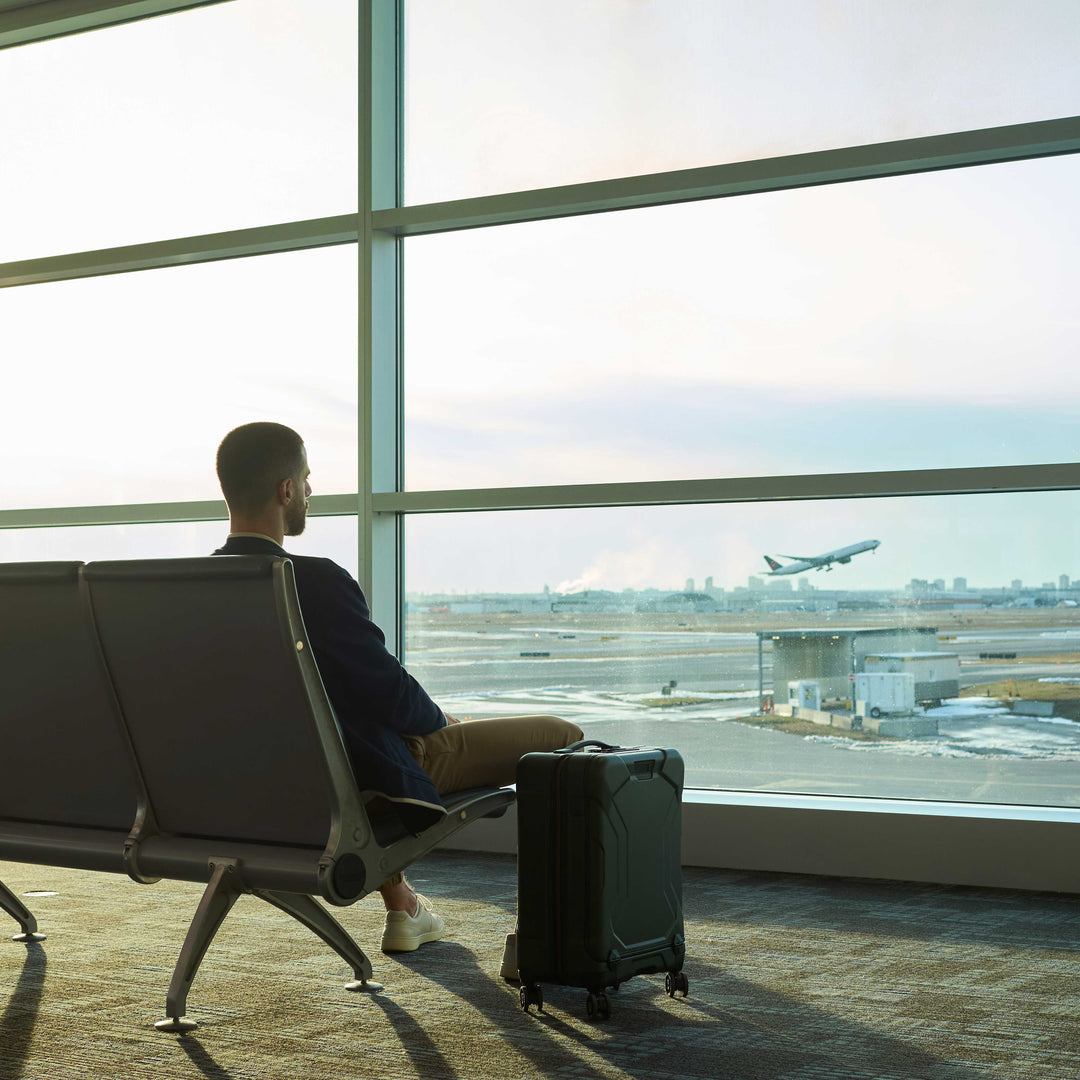 Man watching airplanes at airport with briggs riley torq international carry on in green