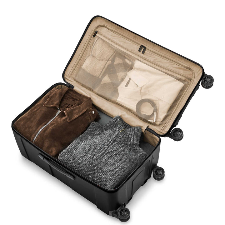 Black Briggs & Riley Torq Medium Hardside Trunk Spinner interior with beige lining packed with sweater and suede jacket