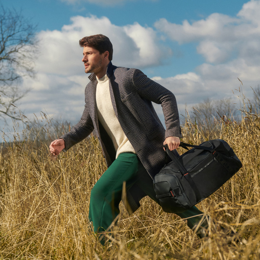 Man runs through field holding his black Briggs & Riley ZDX Large Travel Duffle by the top grab handle