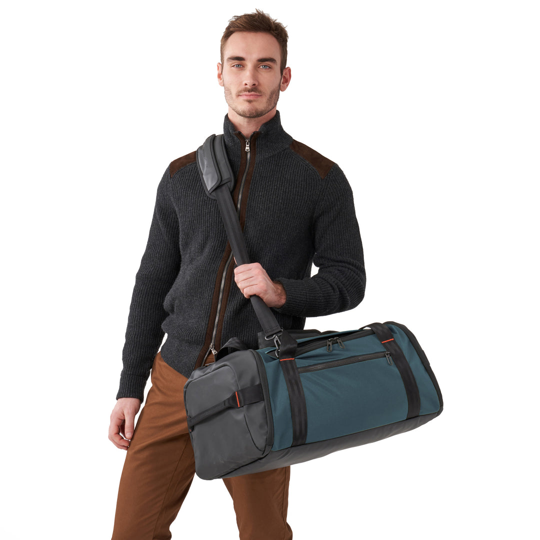 Man in grey sweaters holds Briggs & Riley ZDX Large Travel Duffle by shoulder strap in color Ocean Turquoise