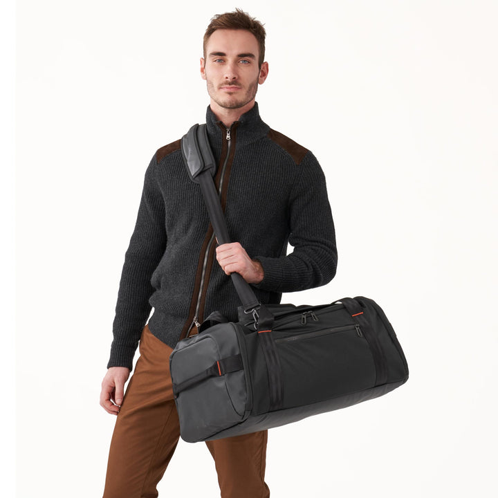 Man holds black Briggs & Riley ZDX Large Travel Duffle crossbody by its padded shoulder strap