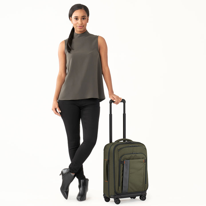 Model stands holding telescoping handle of Olive green Briggs & Riley ZDX International 21" Carry-On Expandable Spinner