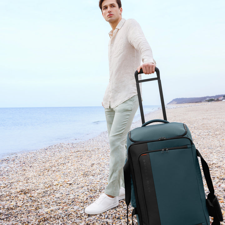 Man Standing at beach with Briggs & Riley ZDX Medium Upright Duffle in color Ocean Blue