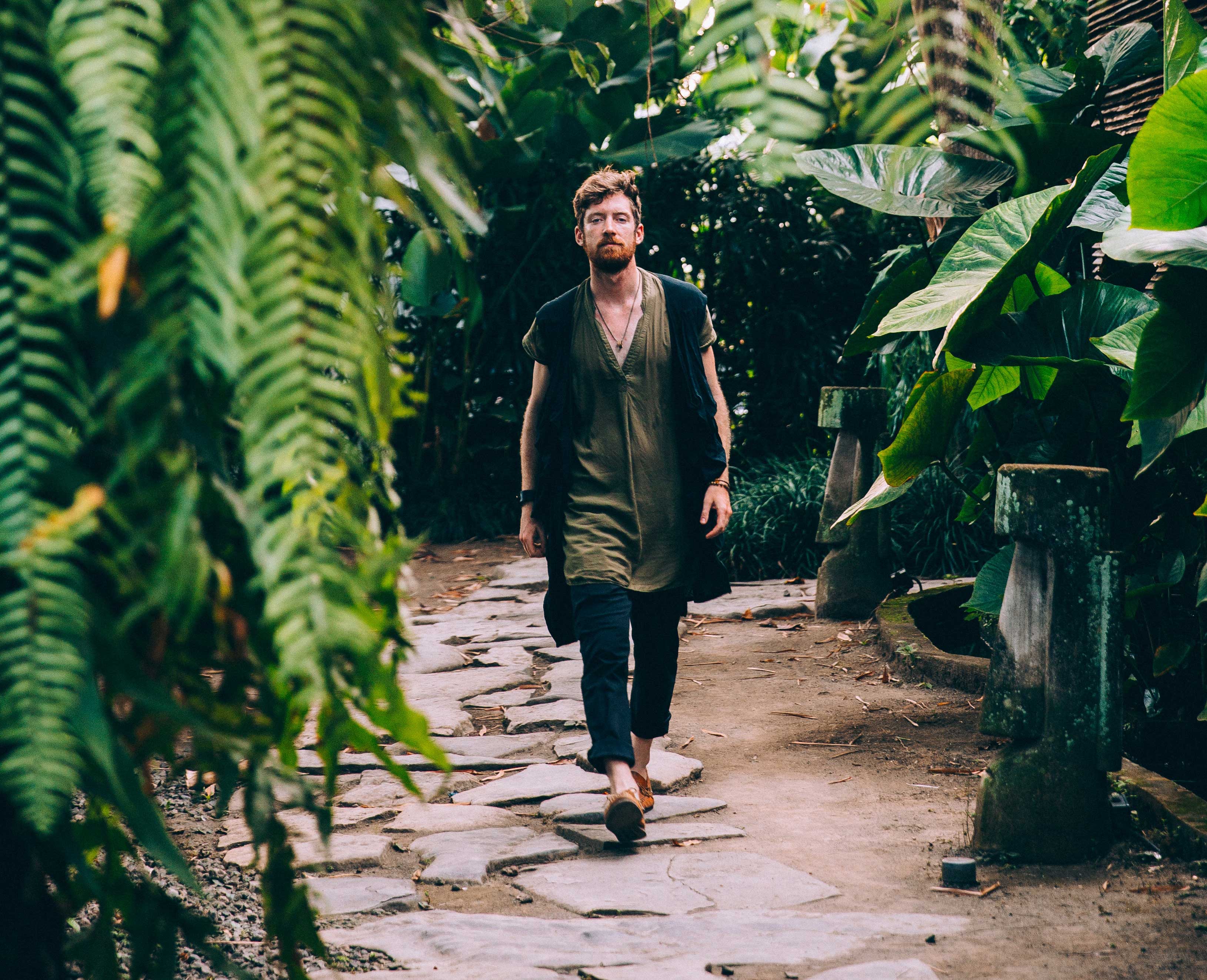 Man walking in shoes through green jungle traveling green