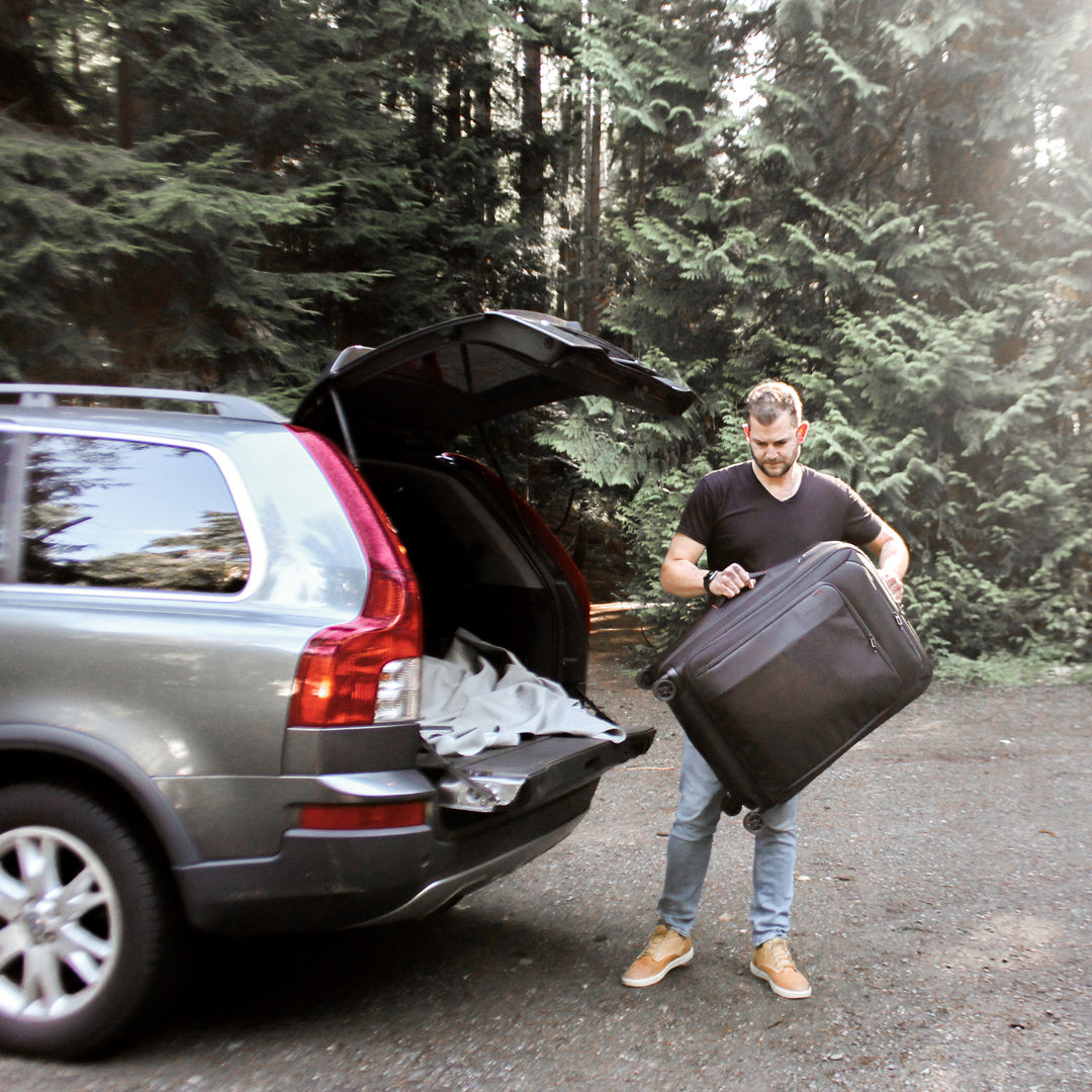 Man loading Briggs & Riley Sympatico Large Expandable Spinner into car with woods in background