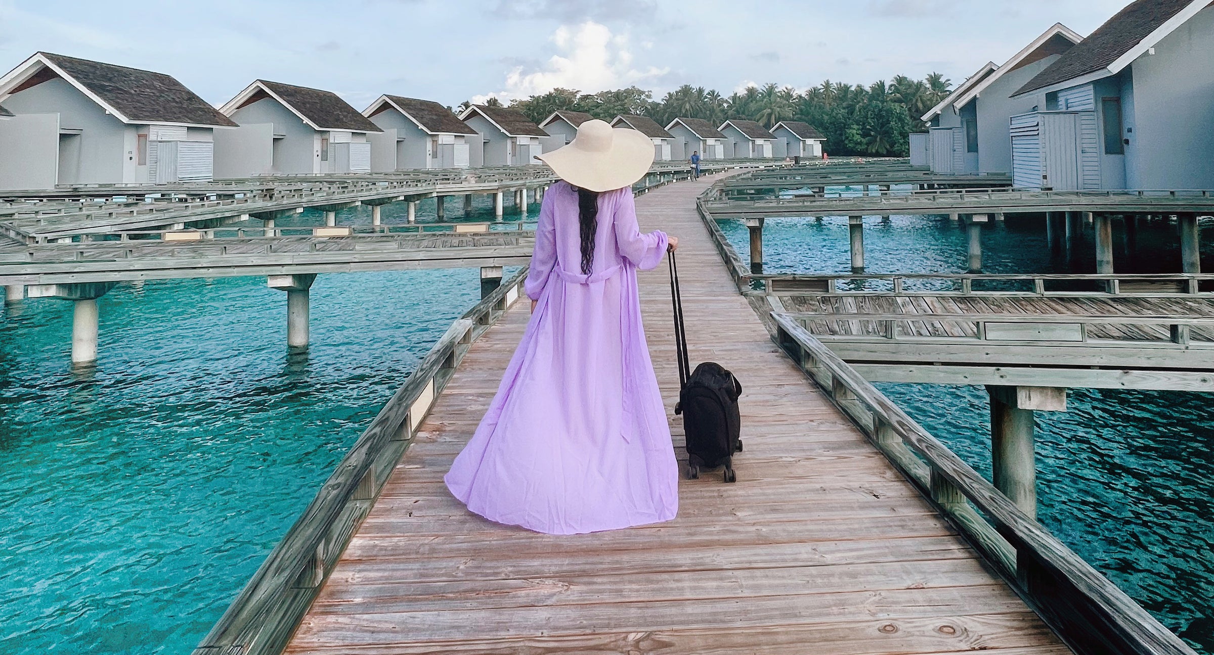 woman in purple robe wheels baseline luggage down dock to hotel room