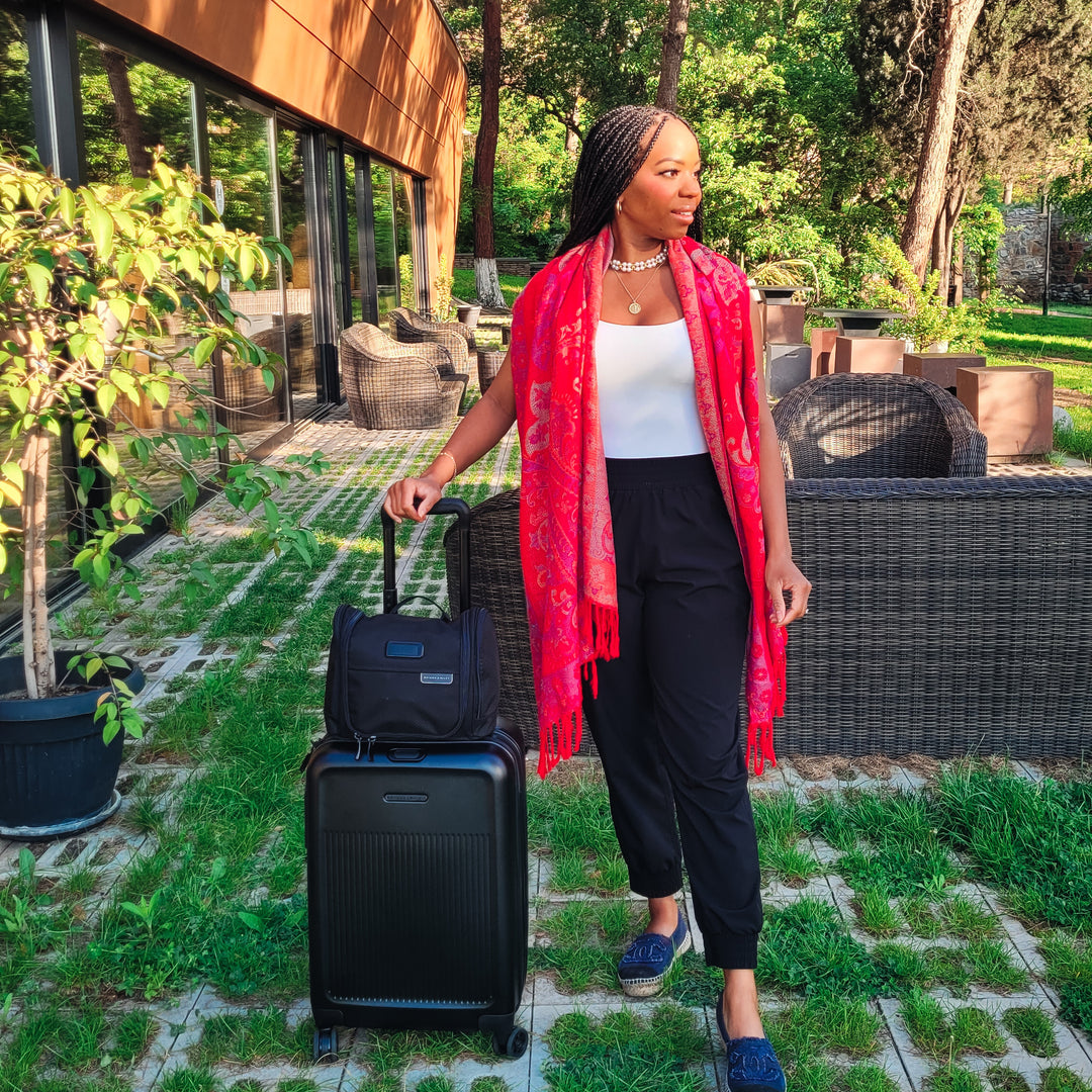 Woman stands outside resort with luggage Briggs & Riley Baseline Underseat Duffle