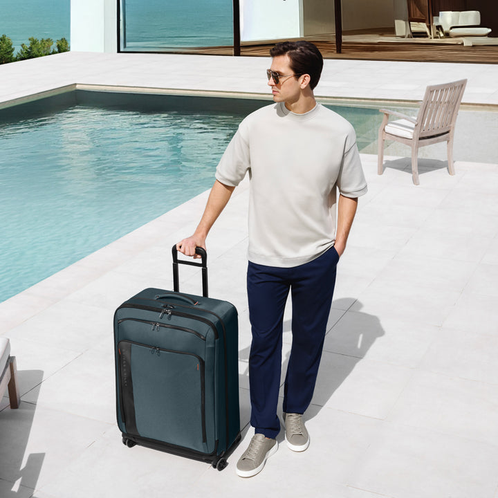 Man stands by swimming pool with ocean view holding his Ocean colored ZDX Large Expandable Spinner Suitcase