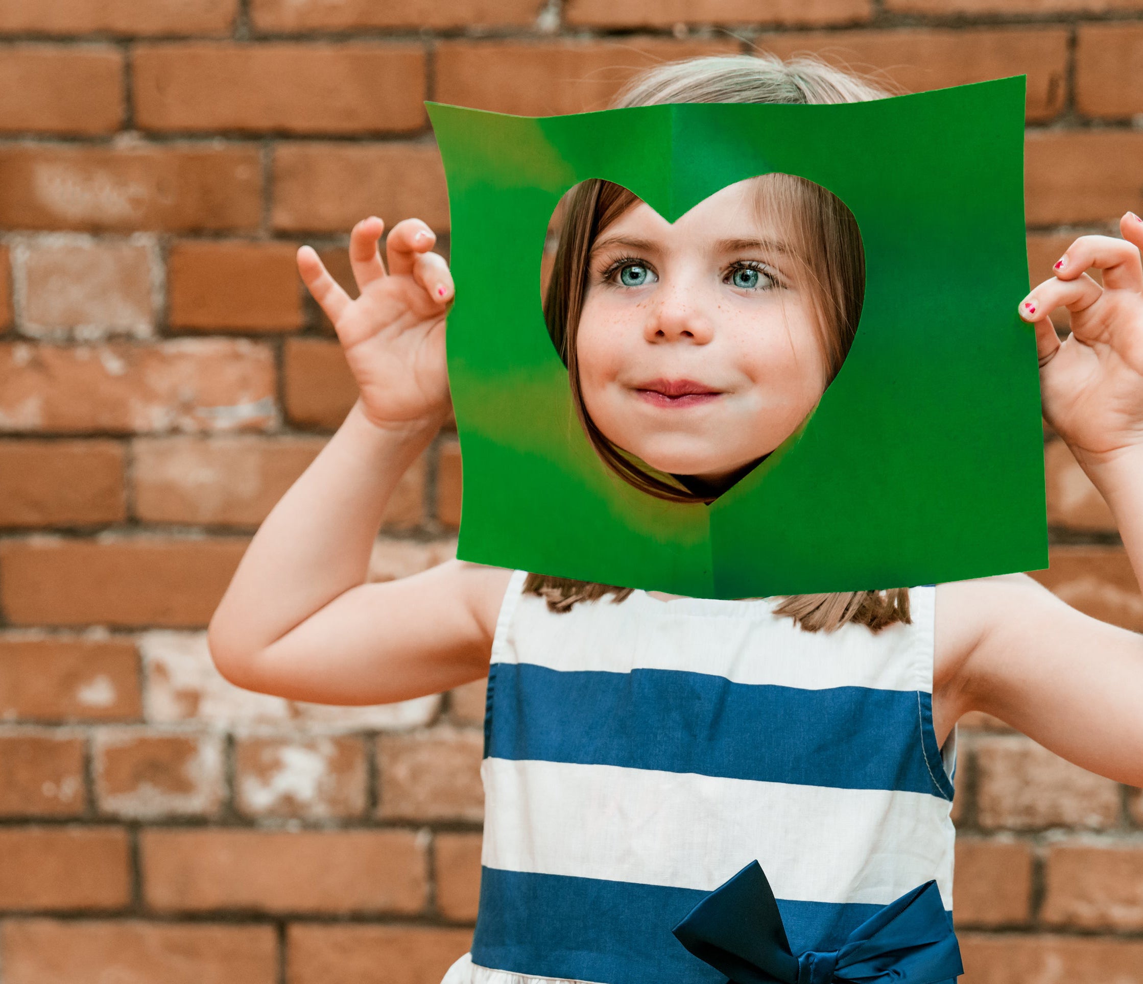 Little foster kid puts face through cut out paper heart