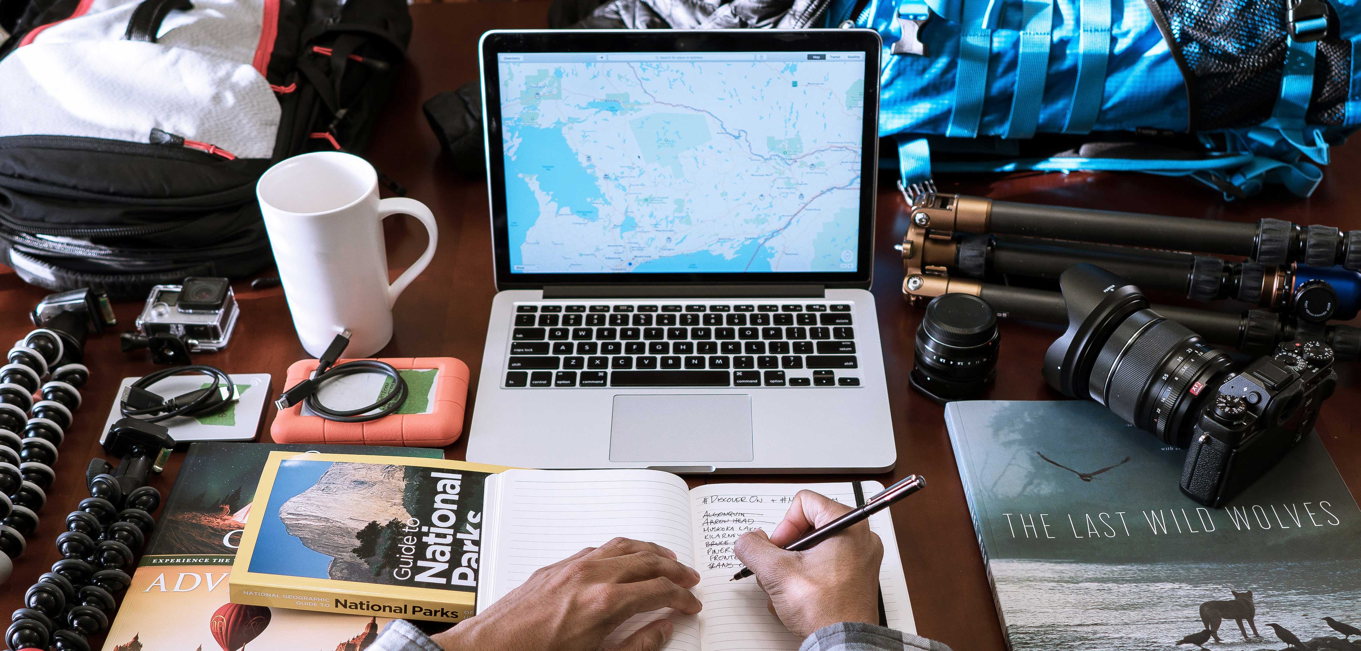 man preparing packing checklist at laptop with lots of supplies